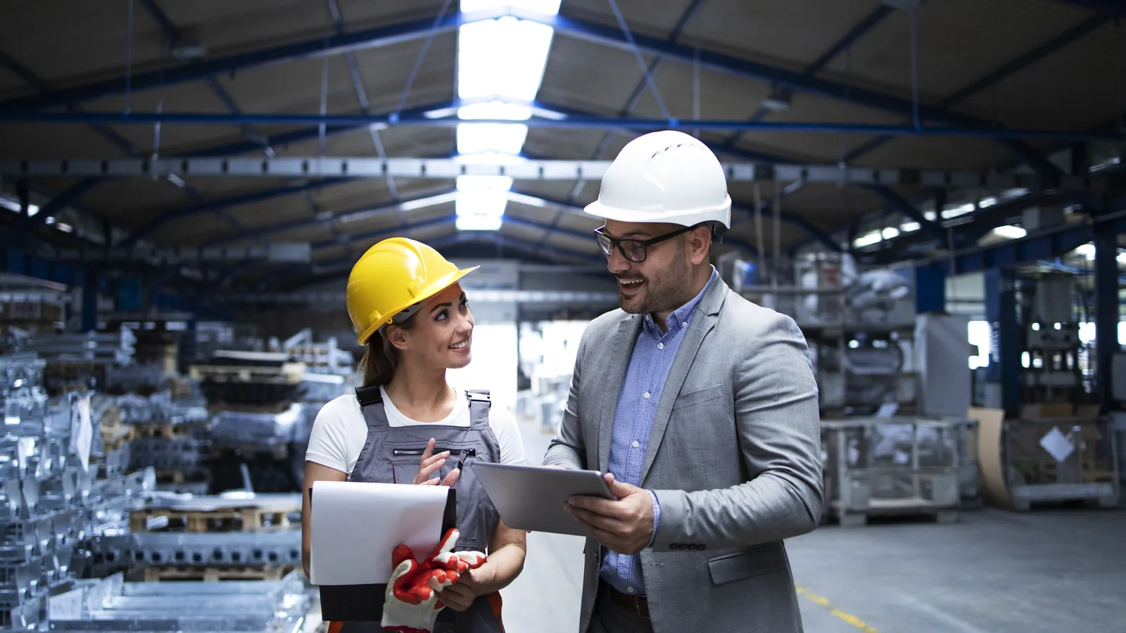 Marketing B2B na prática: como fazer passo a passo 3 Gestor e profissional de produção analisando resultados em um tablet dentro de galpão industrial