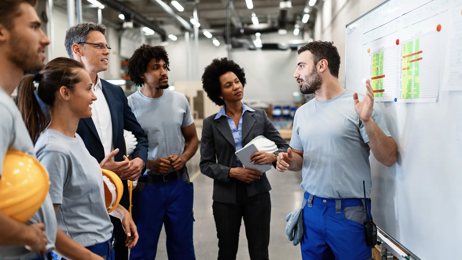 Marketing B2B na prática: como fazer passo a passo 2 Grupo de gestores e profissionais técnicos discutindo um plano em quadro dentro de uma fábrica