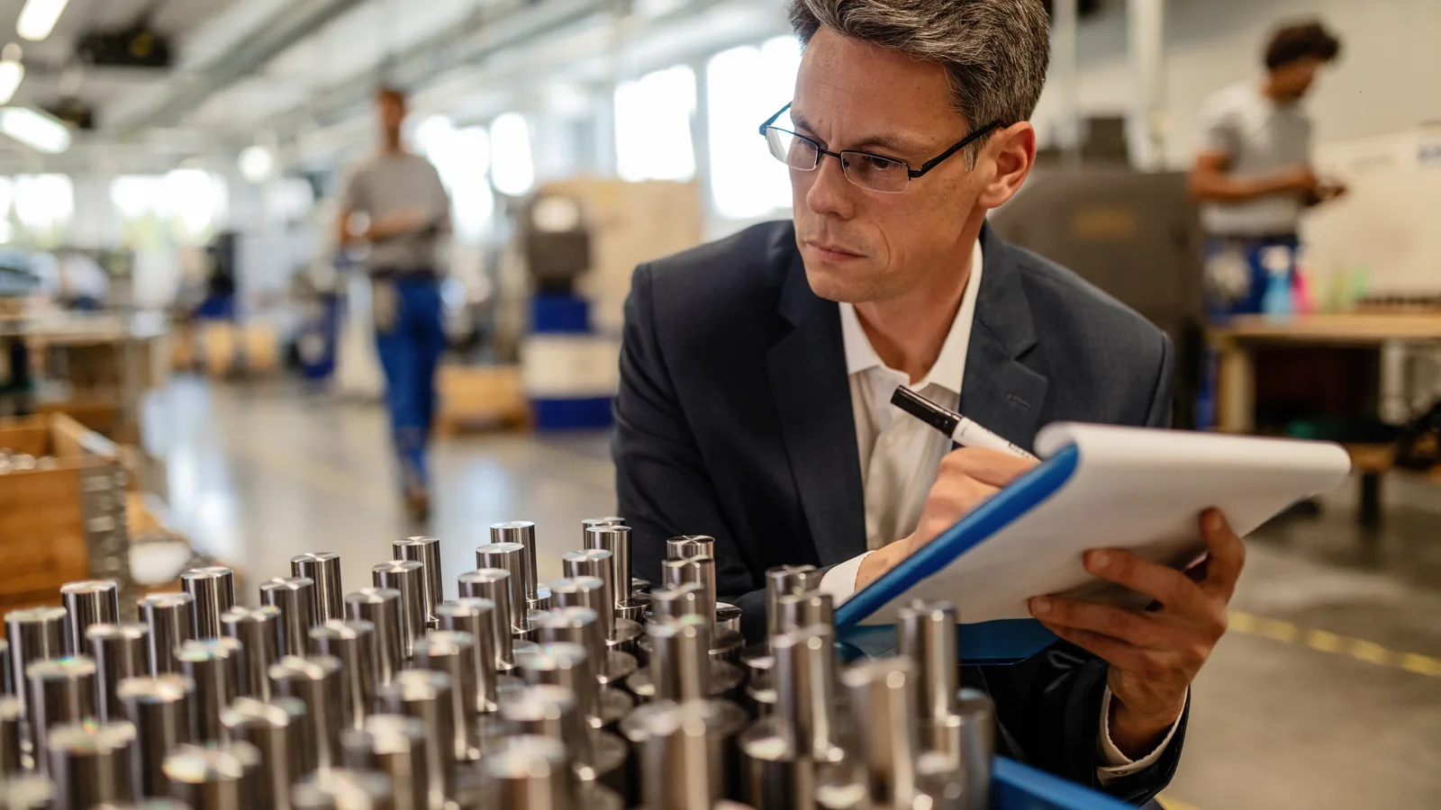 Como vender para grandes empresas e passar na homologação 2 Inspetor de qualidade avaliando peças metálicas usinadas e registrando em prancheta dentro da fábrica